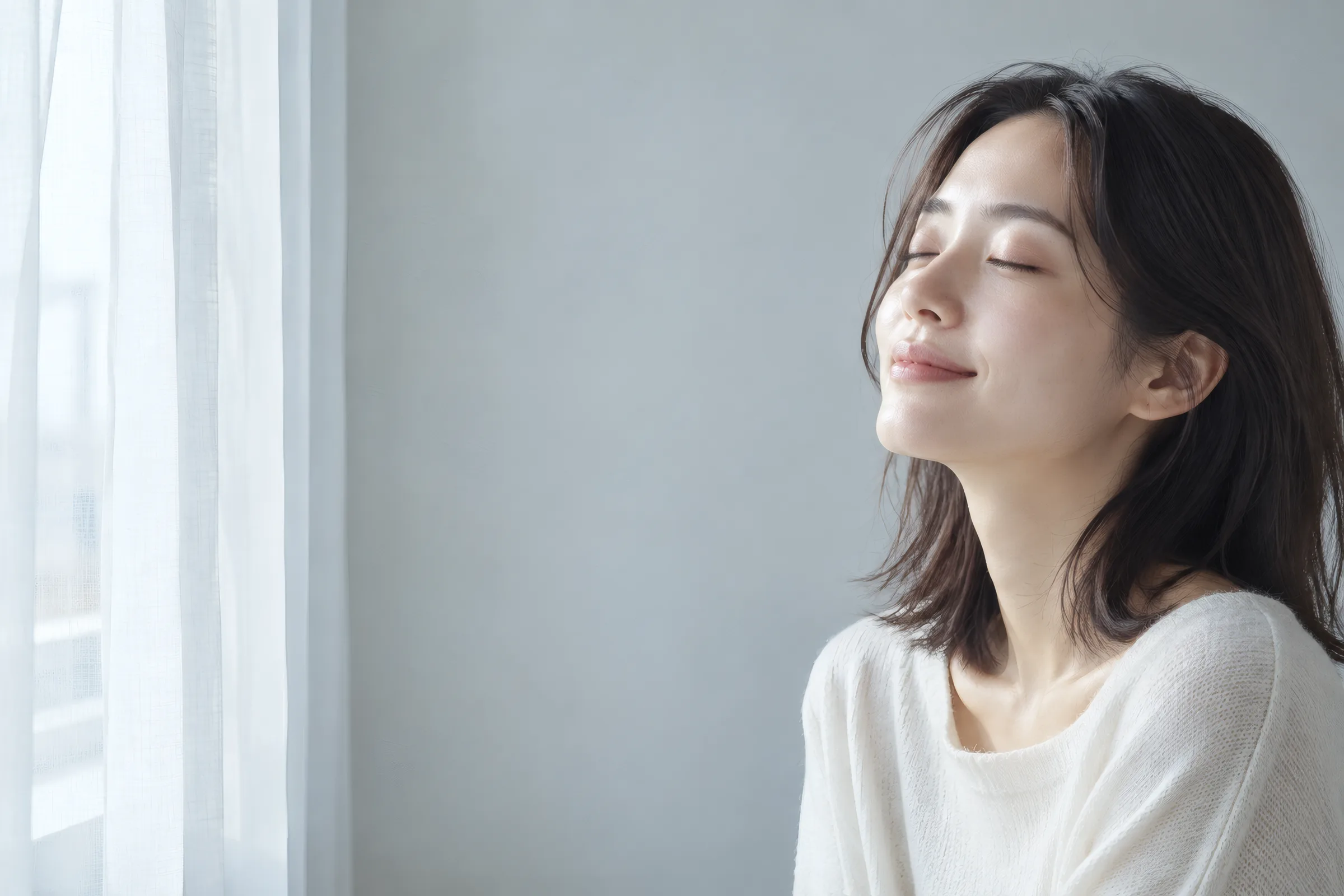窓辺で目を閉じてくつろぐ女性